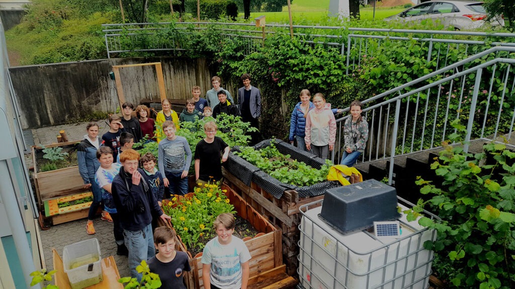 Schüler in Gemeinschaftsgarten mit Hochbeeten und Pflanzen
