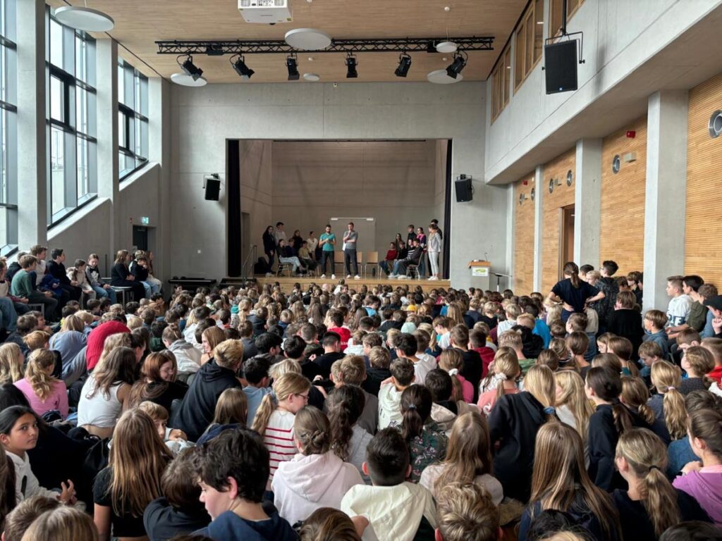 Schulkinder versammeln sich in großer Aula Veranstaltung