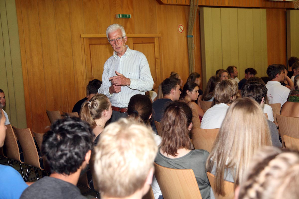Älterer Mann spricht vor Publikum im Saal.